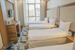 Ein Hotelzimmer mit zwei Betten, einem Schreibtisch, einem Spiegel und einem Fenster mit Blick auf die Stadt.