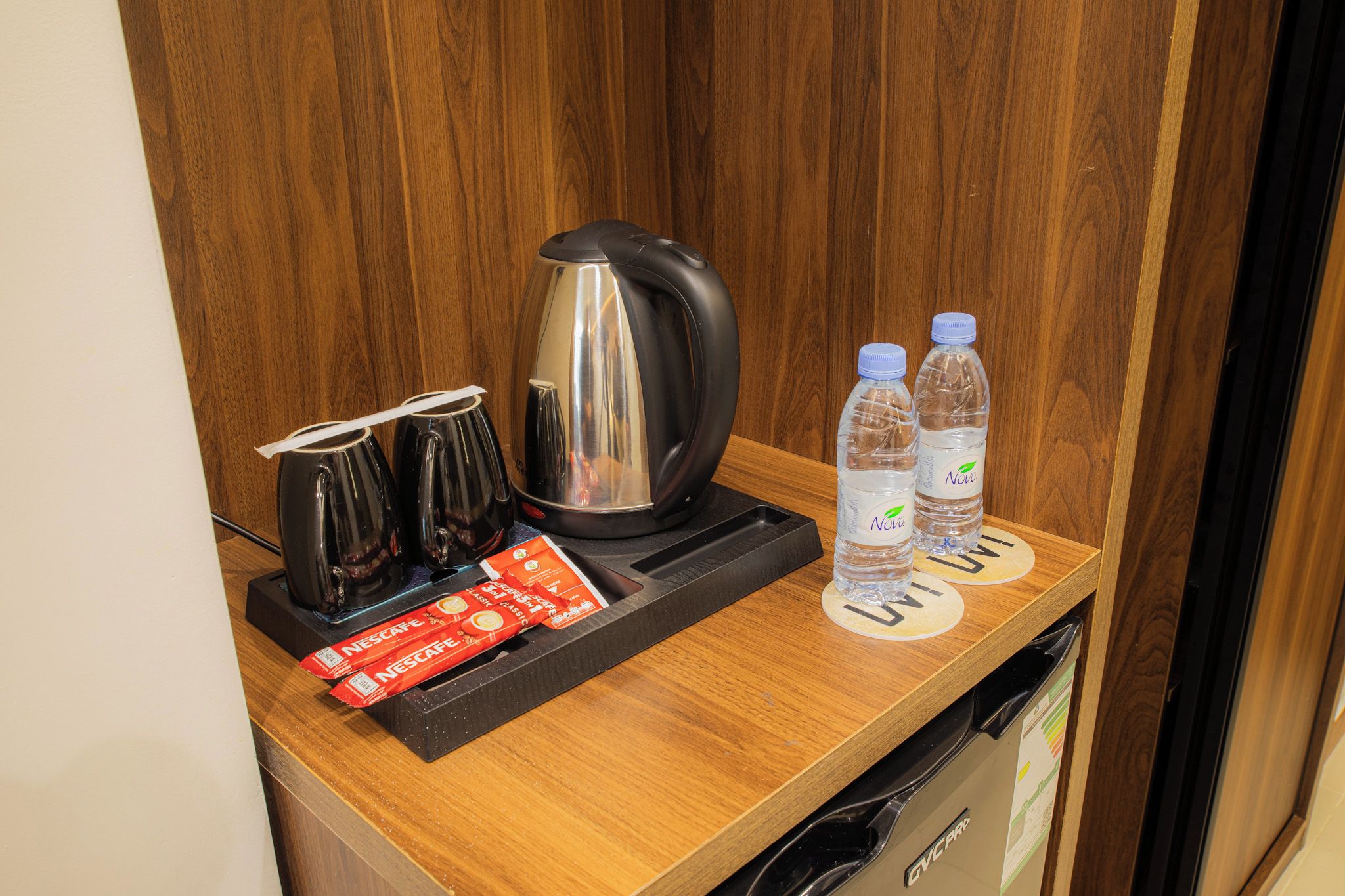 A kitchenette with a coffee maker, two water bottles, and two packets of Nescafe coffee.