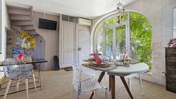 Ein Zimmer mit Esstisch, Stühlen, einem Fernseher und einer Tür zu einem Balkon mit Blick auf Grünflächen.