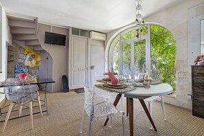 Habitación con una mesa de comedor, sillas, televisor y una puerta que da a un balcón con vistas a zonas verdes.
