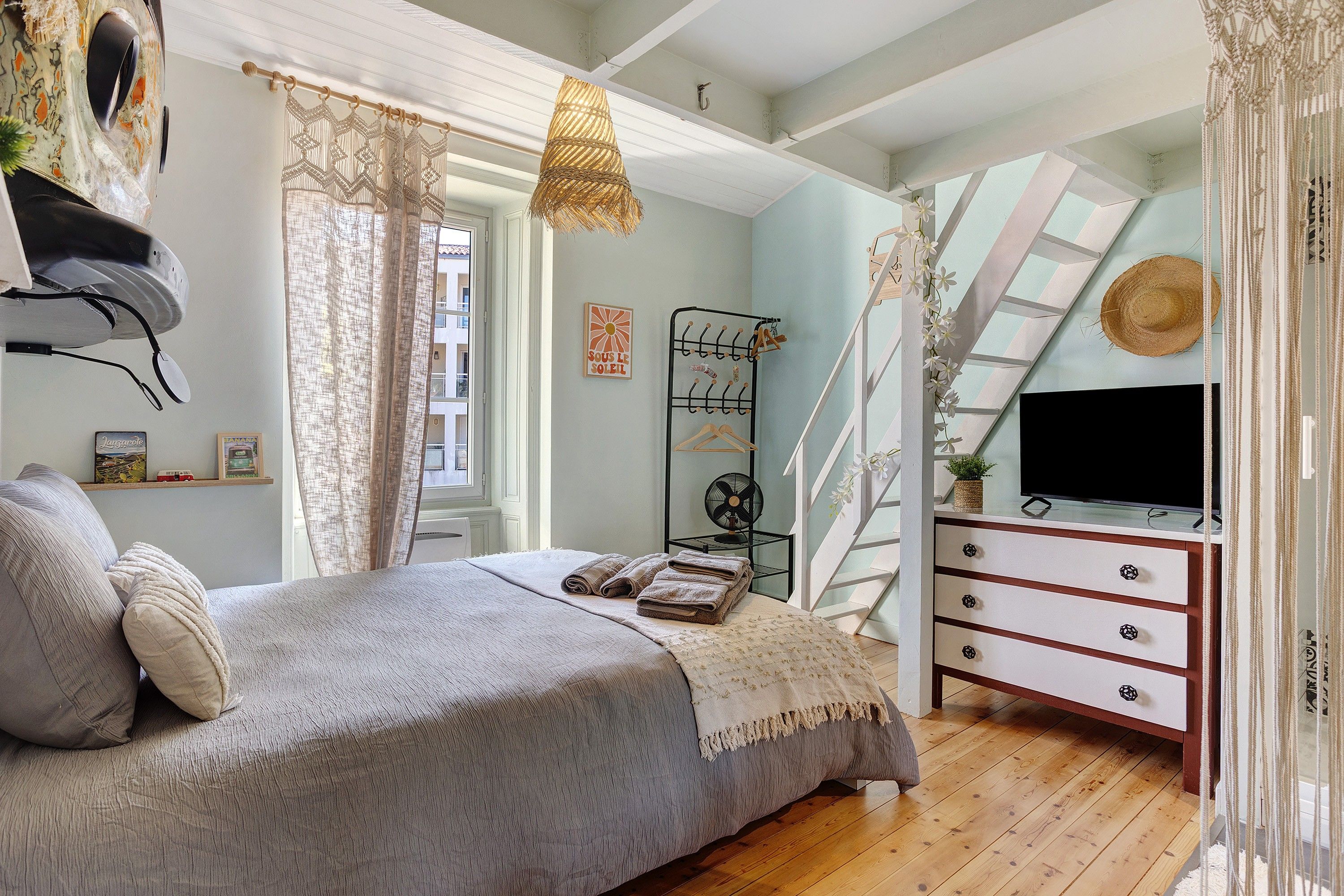 Ein Schlafzimmer mit Bett, Kommode, Fernseher und einem Fenster mit Vorhängen.