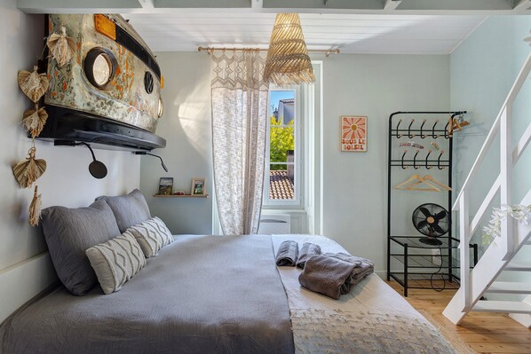 Une chambre à coucher avec un lit, un luminaire suspendu, une fenêtre avec des rideaux et un étendoir fixé au mur.