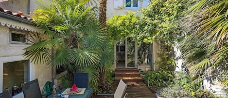 A patio with a table set for dining, surrounded by lush greenery and a palm tree.