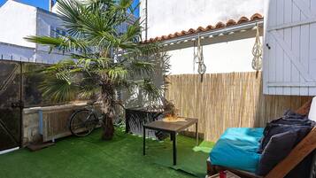 Eine Terrasse mit künstlichem Rasen, einem Tisch mit Flasche und Glas, einem Fahrrad und einem Holzzaun.