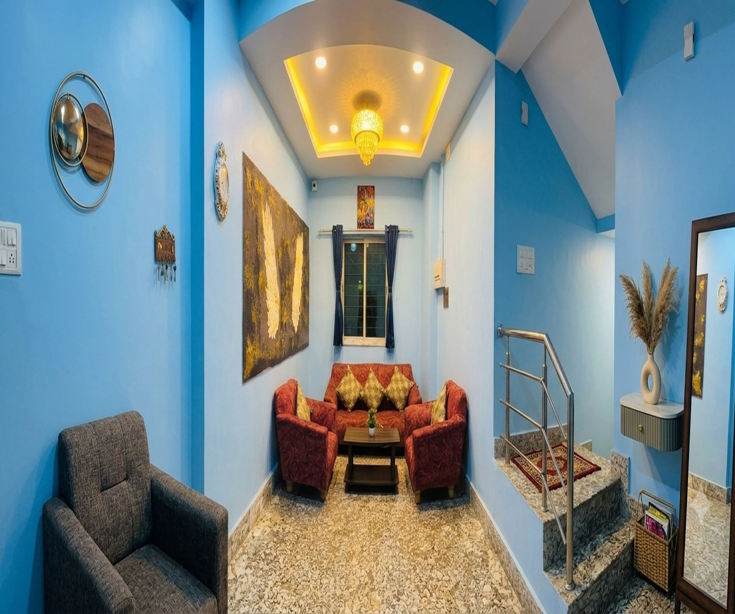Una habitación con pared azul, un sofá, una silla, una mesita y una escalera.