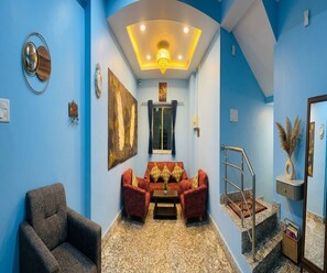 Une pièce avec un mur bleu, un canapé, une chaise, une petite table et un escalier.