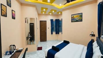 Habitación de hotel con cama, escritorio, silla, ventilador de techo y obras de arte en las paredes.