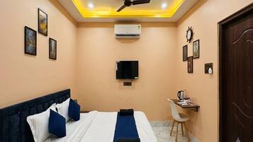 A hotel room with a bed, a desk, a television, and an air conditioning unit.