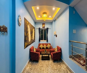 Une pièce avec un mur bleu, un ensemble de meubles de salon rouge, un lustre et une fenêtre avec des rideaux.
