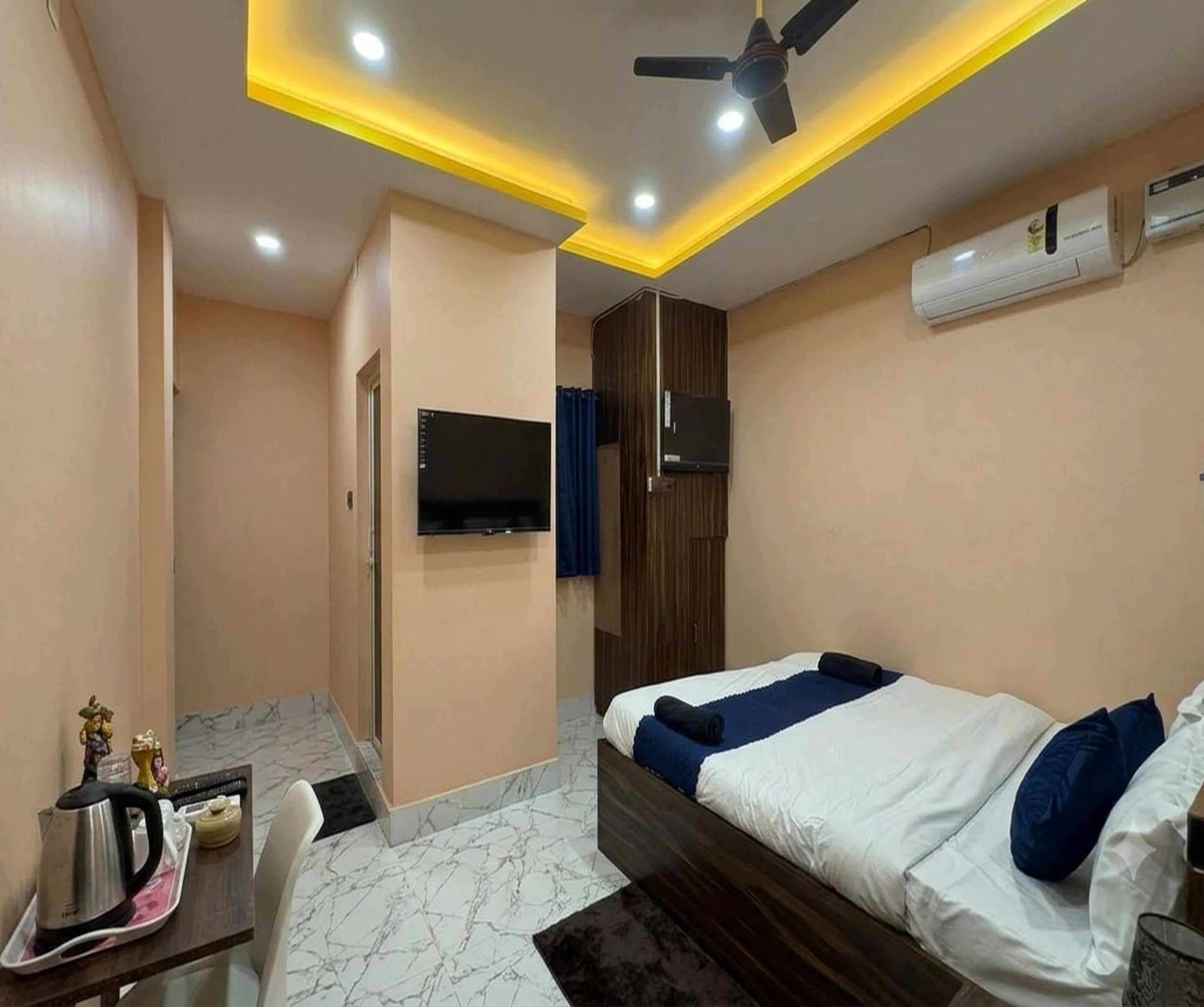Una camera da letto con un letto, una scrivania con un bollitore, una televisione e un condizionatore d'aria.