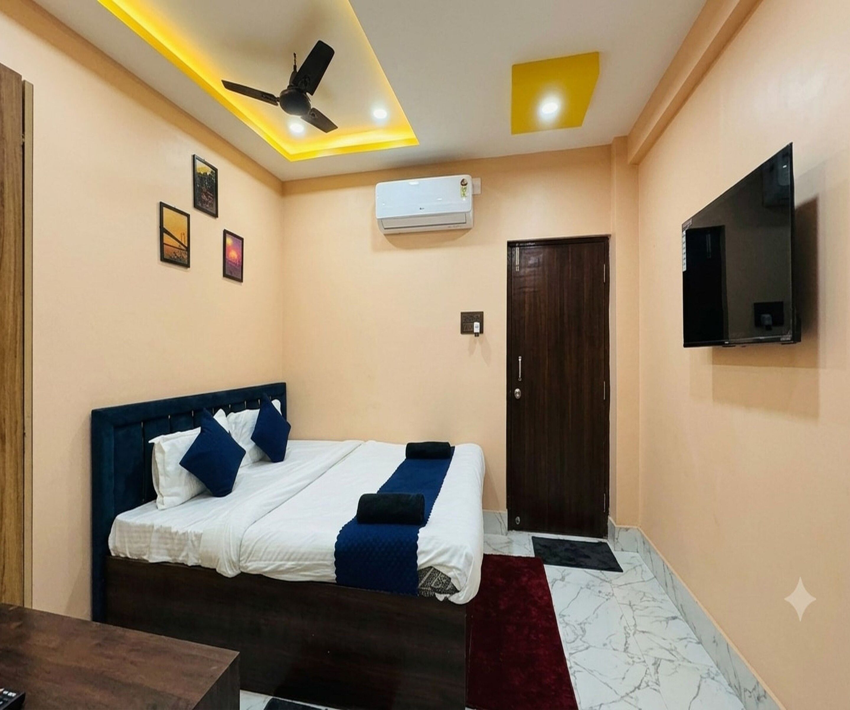 A hotel room with a bed, a ceiling fan, an air conditioning unit, a TV mounted on the wall, and a door.