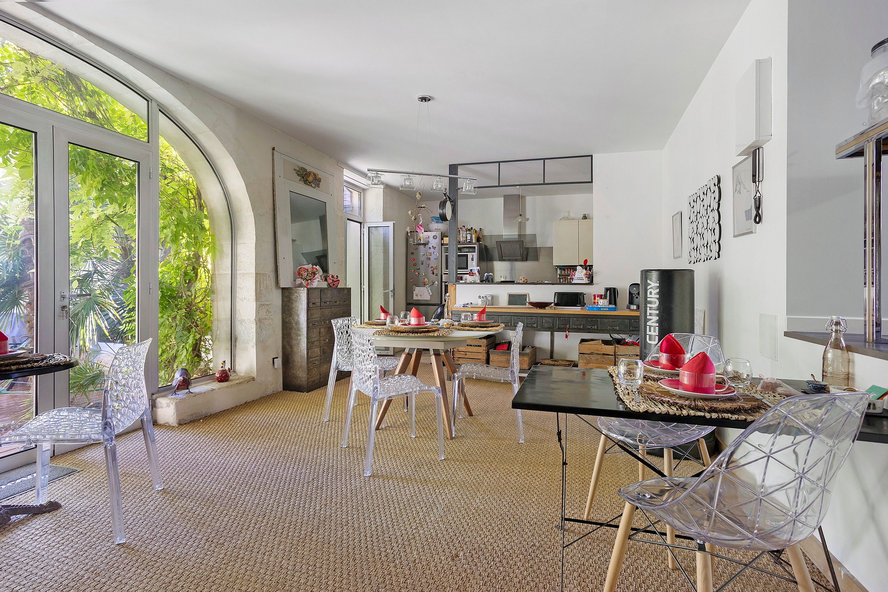 A modern kitchen with a dining area, large windows, and a view of greenery.