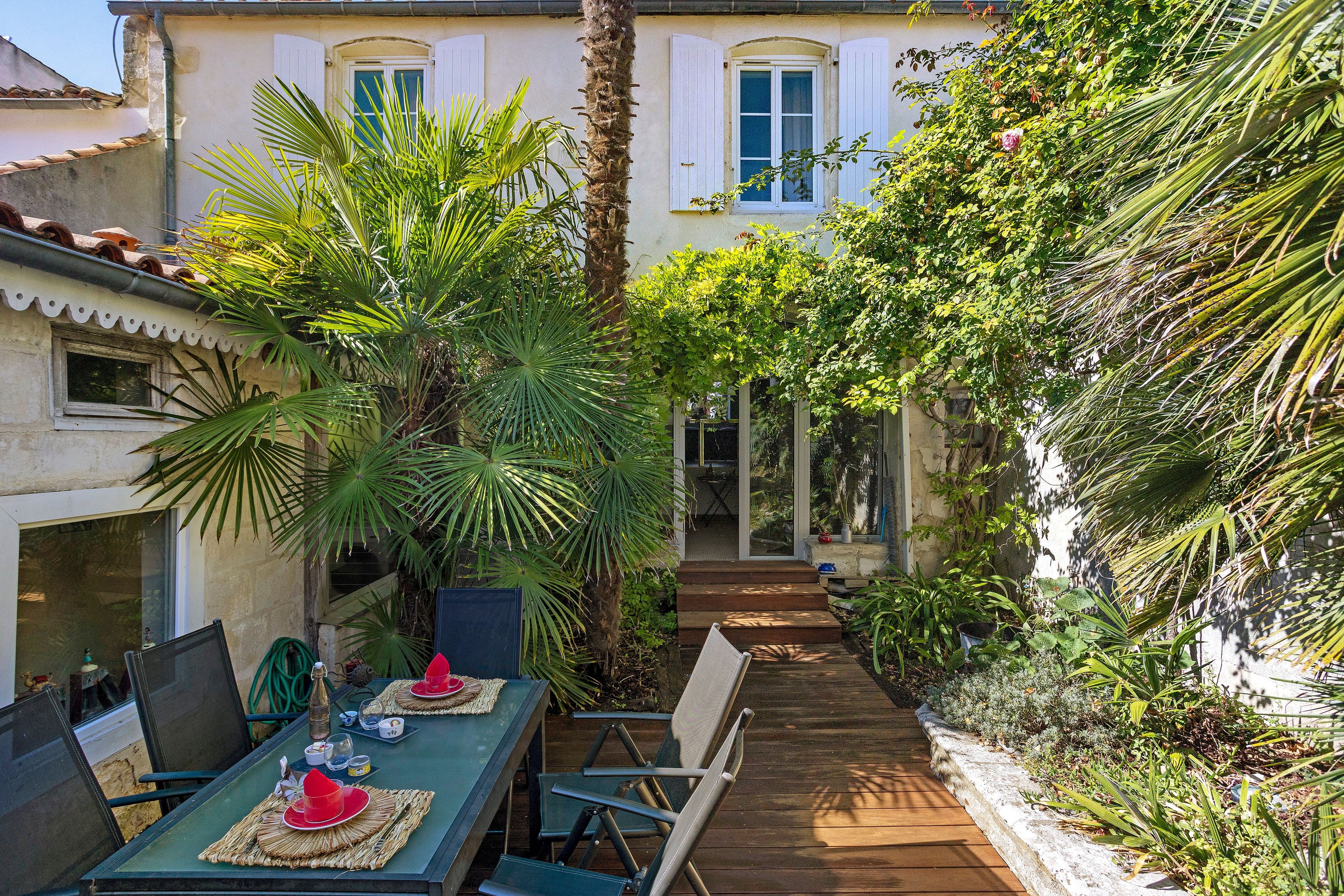 A patio with a table set for dining, surrounded by lush greenery and a palm tree.