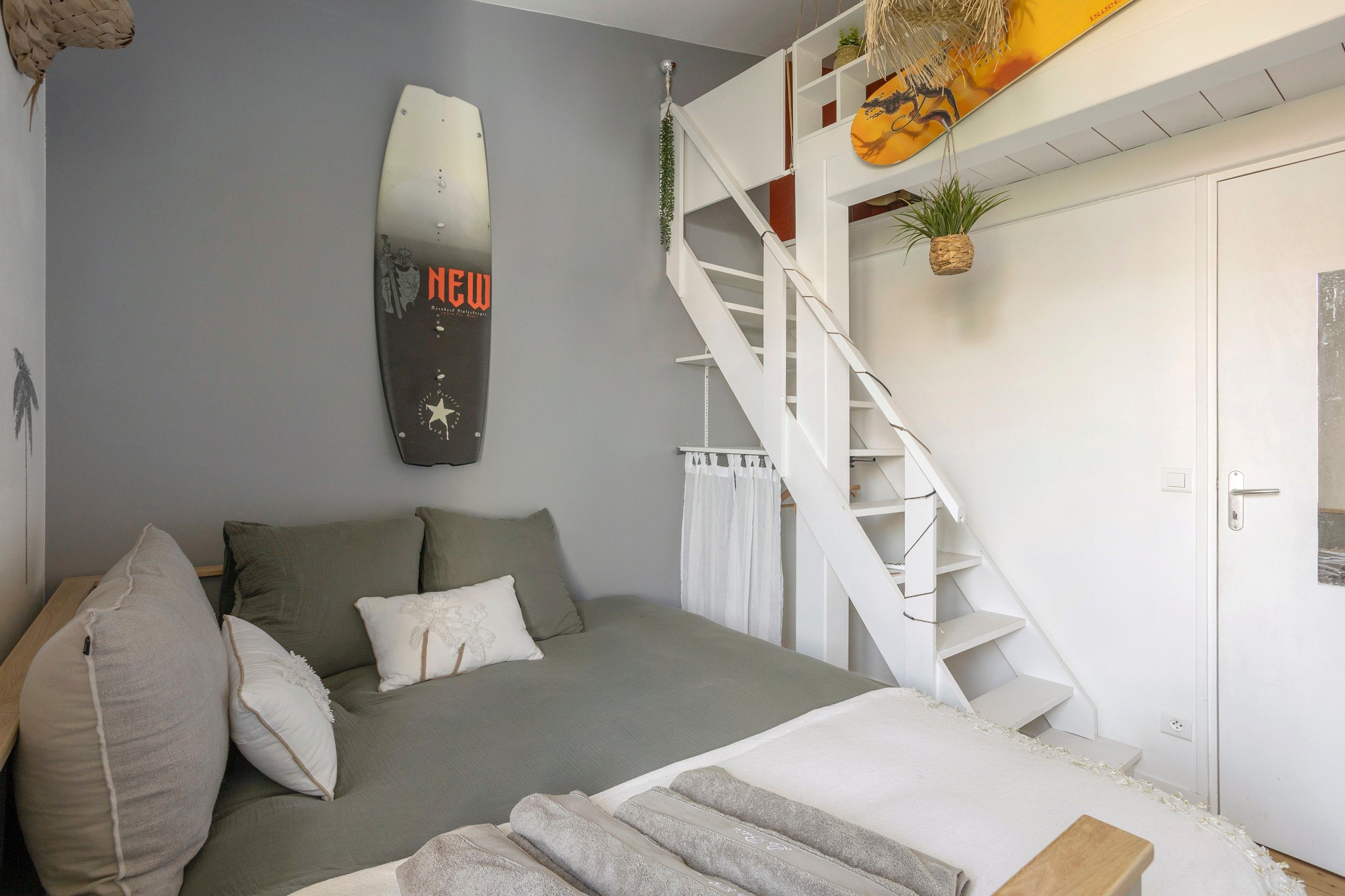 Une chambre avec un lit, un escalier blanc et un miroir fixé au mur.