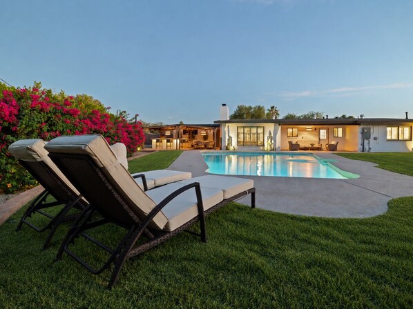 Ein Wohnhaus mit Schwimmbad, Sitzgelegenheit im Freien und einem gepflegten Rasen.