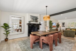 Ein modernes Wohnzimmer mit Essbereich, ausgestattet mit einem Kamin, einem großen Spiegel und einer zeitgemäßen Leuchte.