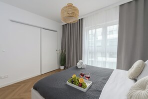 A modern bedroom with a bed, a bedside table with a fruit bowl and glasses, a potted plant, and a view of the city through large windows. - Lumina 4-room Apart w/ Parking & Balcony (Warszawa)