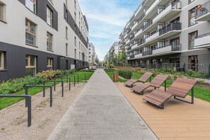 A pathway leading to a modern apartment building with balconies and a garden area with benches. - Lumina 4-room Apart w/ Parking & Balcony (Warszawa)