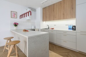 A modern kitchen with a central island, wooden cabinets, and a white countertop. - Lumina 4-room Apart w/ Parking & Balcony (Warszawa)