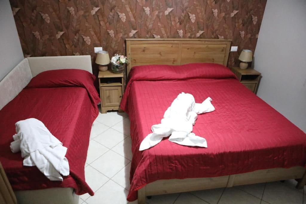 Deux lits simples avec une literie rouge et des têtes de lit en bois, dans une chambre dont le papier peint est à motifs.