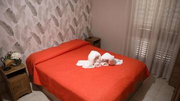 A hotel room with a bed, a nightstand, a small table with a vase, and a window with curtains.