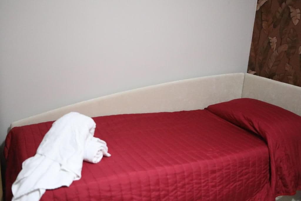 A single bed with a red bedspread and a white blanket draped over the side.