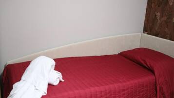 A single bed with a red bedspread and a white blanket draped over the side.