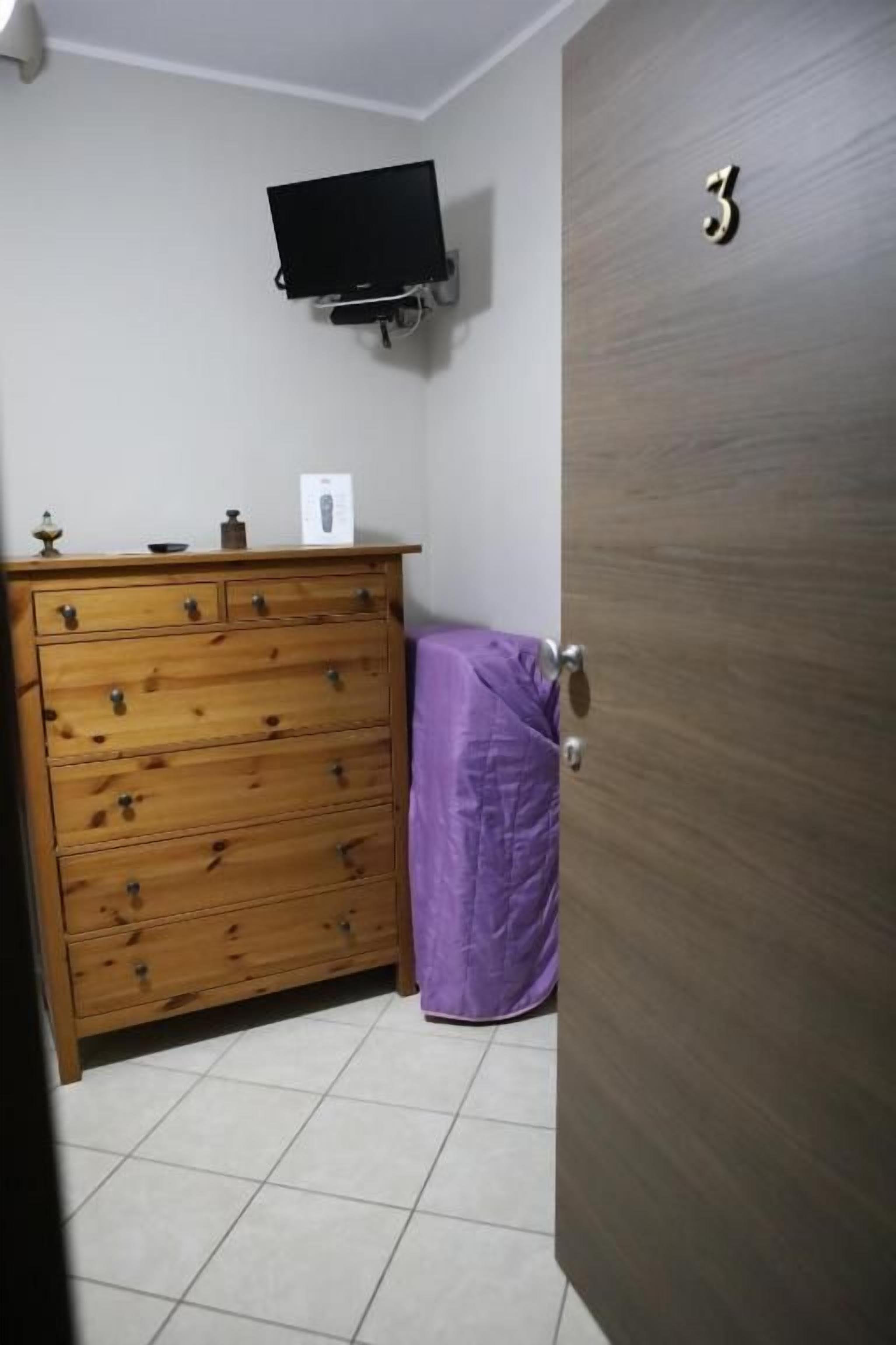 A room with a wooden dresser, a television mounted on the wall, and a door with a number.