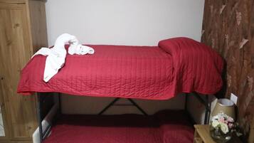 A bunk bed with a red bedspread and pillows, a wooden wardrobe, and a small bedside table with a vase of flowers.