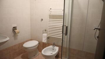 Une salle de bain comprenant des toilettes, un bidet, un lavabo et une douche à parois de verre.