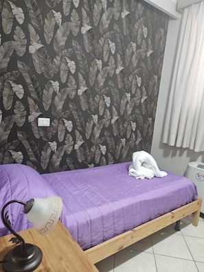 Cama de solteiro com colcha roxa, cabeceira de madeira e parede com padrão de folhas.