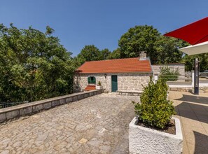 A stone building with a red roof, a green door, and a small garden area with a potted plant. - Villa Pax - Four Bedroom Villa With Outdoor Pool (Lovreć)