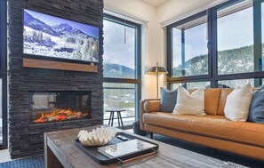 Ein gemütliches Wohnzimmer mit Kamin aus Stein, einer Ledersofa und einem großen Fenster mit Blick auf schneebedeckte Berge.