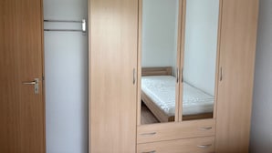 Un armario de madera con puerta espejada, una cama pequeña y un cajón extraíble.