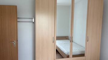 Un armario de madera con puerta espejada, una cama pequeña y un cajón extraíble.