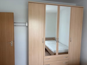 Ein Holzkleiderschrank mit Spiegel, ein kleines Bett und eine ausziehbare Schublade.