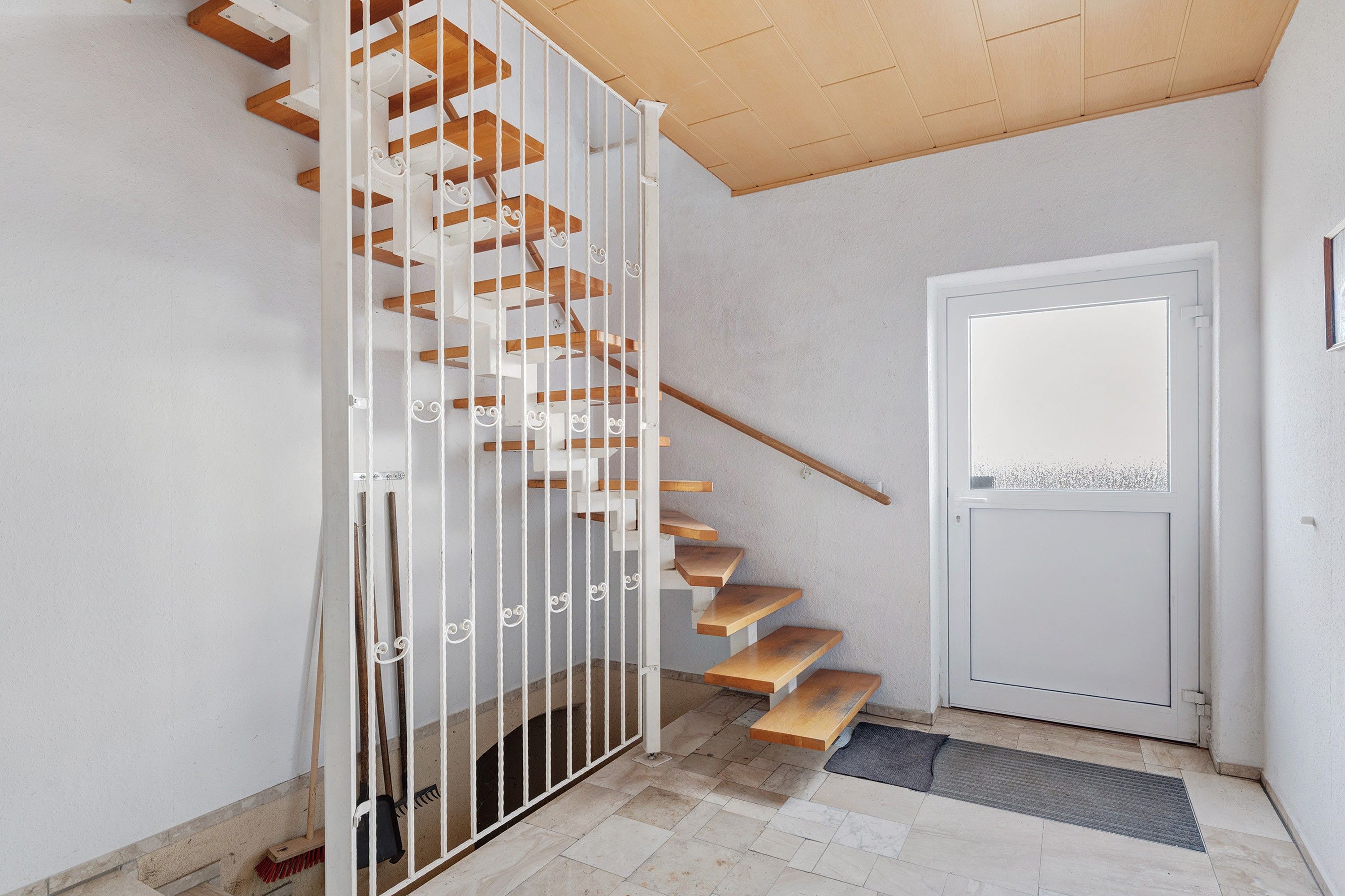 Una escalera con escalones de madera y barandillas blancas, que conduce a una puerta con un ventanal.
