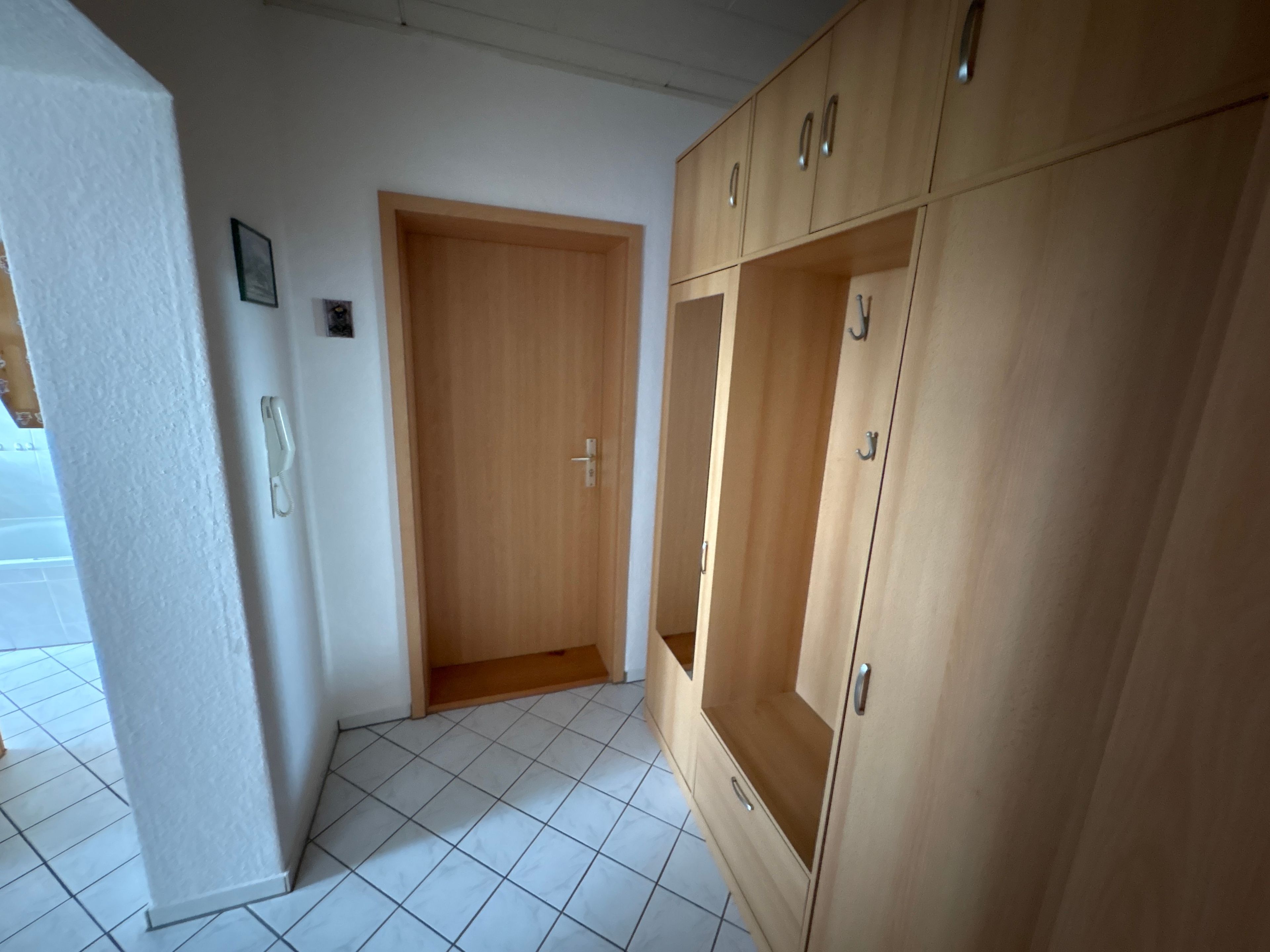 Een kamer met een houten garderobe, een deur en betegelde vloer.