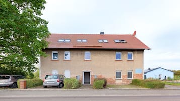 A two-story residential building with a red-tiled roof, multiple windows, and a parked car in front.