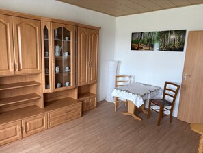 Une pièce avec un meuble en bois, une table avec des chaises et un tableau accroché au mur.