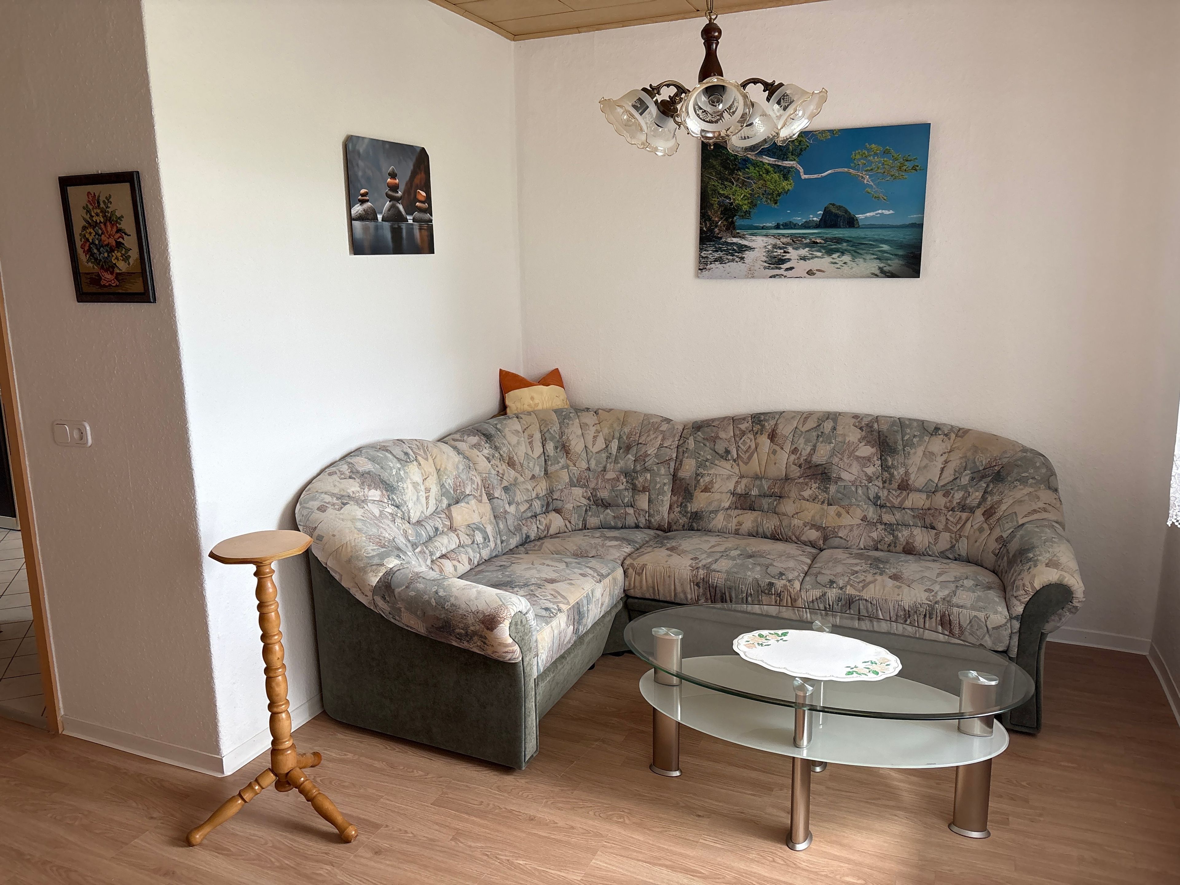 Ein Wohnzimmer mit einem gebogenen Ecksofa, einem Glastisch, einem Holznachttisch und einer Kronleuchter.