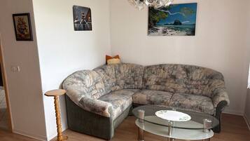 Ein Wohnzimmer mit einem gebogenen Ecksofa, einem Glastisch, einem Holznachttisch und einer Kronleuchter.