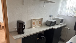 Una cocina compacta con cafetera, microondas y salpicadero de azulejos.