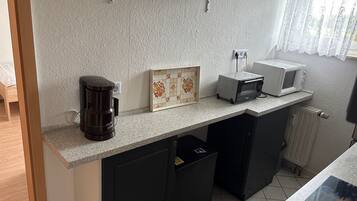Una cocina compacta con cafetera, microondas y salpicadero de azulejos.