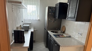 Una cocina compacta con cafetera, refrigerador, lavamanos y ventana con cortinas.