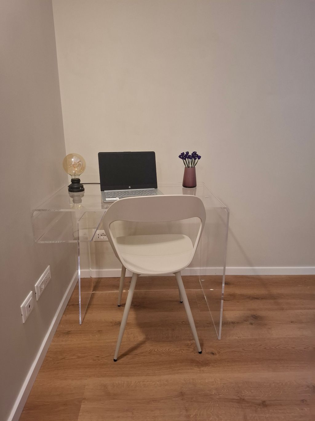 Un bureau bien rangé avec un ordinateur portable, une chaise, un vase de fleurs et une ampoule.