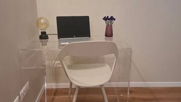 A clear desk with a laptop, a chair, a vase with flowers, and a light bulb.