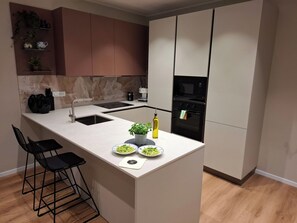 Una cocina moderna con una isla central, taburetes de bar, horno empotrado y microondas.