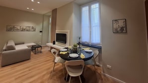 Een moderne woonkamer met een bank, een eettafel gedekt voor twee personen en een tv aan de muur.