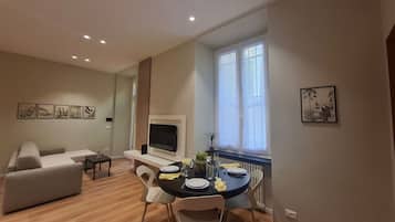 Una sala moderna con un sofá, una mesa de comedor para dos personas y un televisor montado en la pared.
